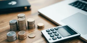Calculator, coins, and laptop on a wooden table.